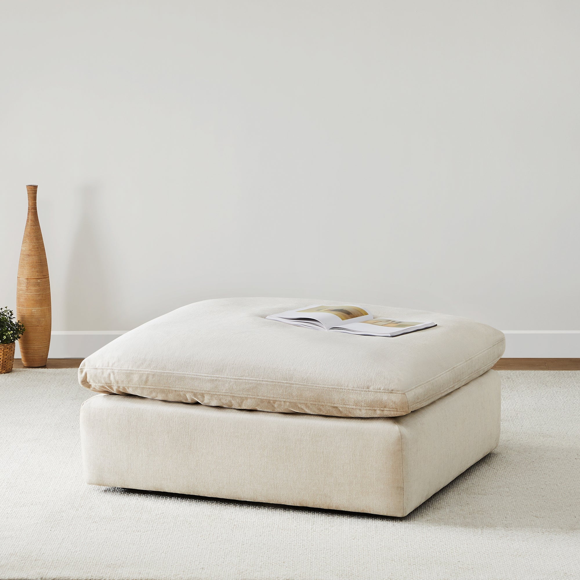 Beige upholstered ottoman, part of the Kenna collection, with a book on top, modern living room furniture.